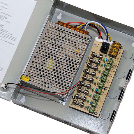 Caja metálica con fuente de alimentación y panel con 9 puertos de conexión, voltaje de salida ajustable ±10%, dimensiones reducidas, refrigeración de la fuente por convección natural y protección contra sobrecargas y sobretensiones.